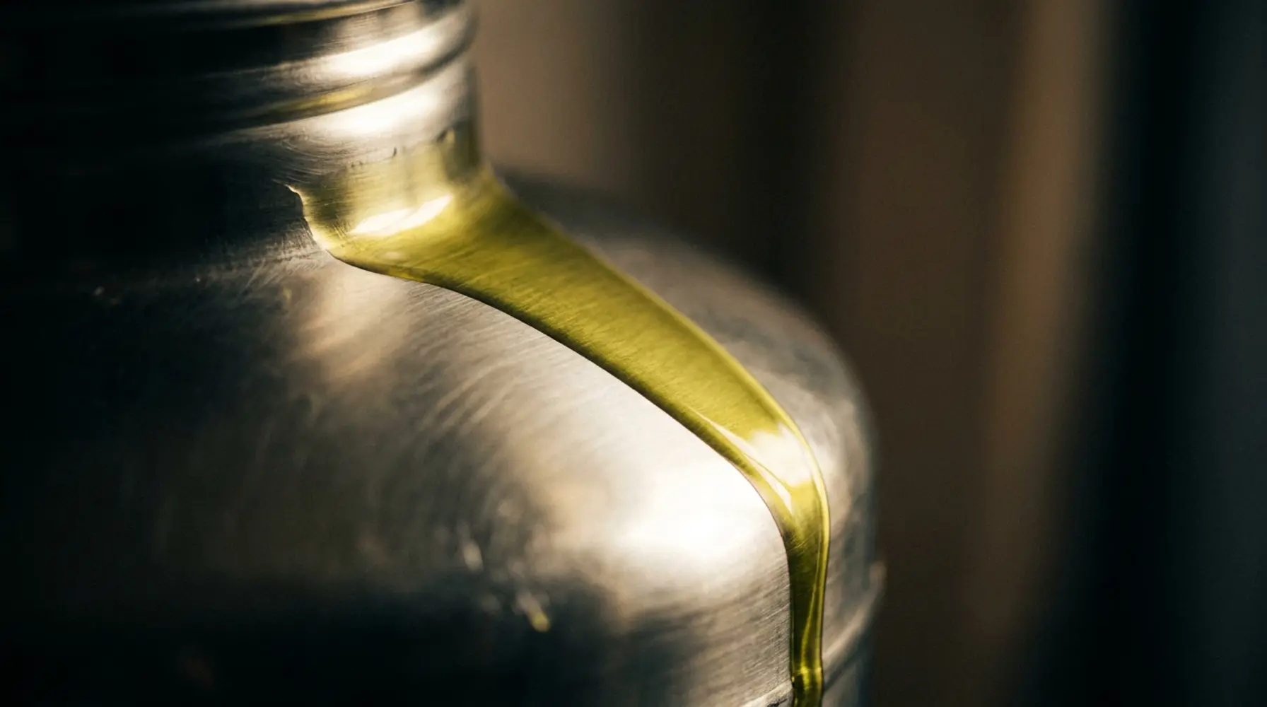First-press olive oil sheeting off a steel tank in raking light.